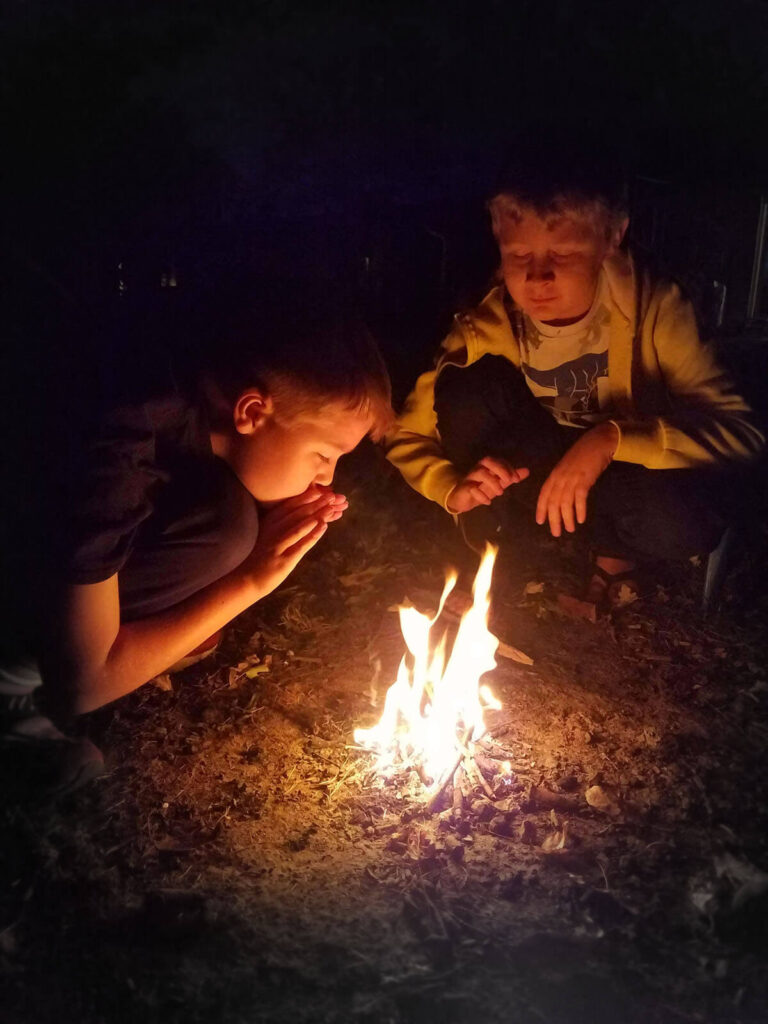 two young boys stoking a tiny campfire at night